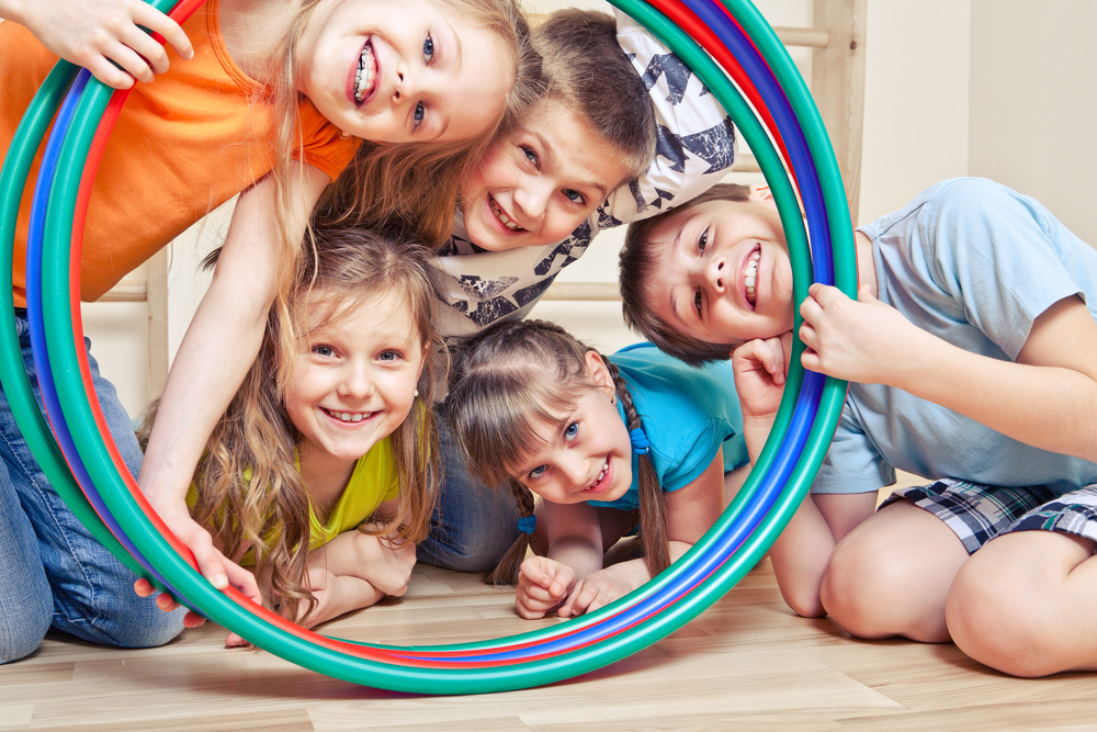 Five cheerful kids looking through hula hoops play